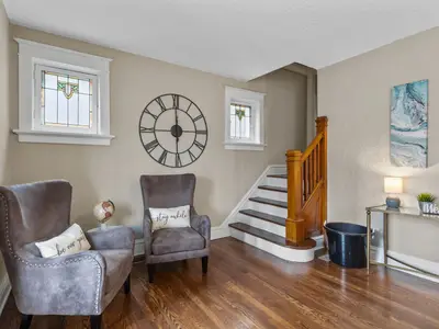 Sitting area with two accent chairs beneath a large wall clock, next to the staircase