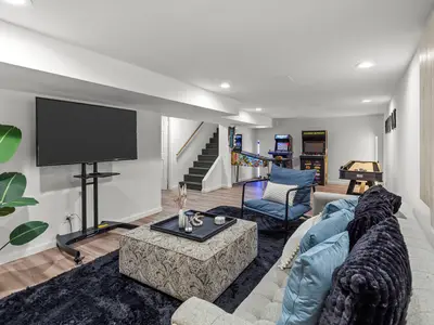 Basement lounge area with sectional sofa, mounted TV, and view toward the arcade games